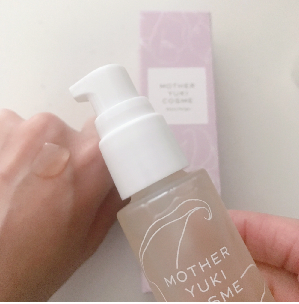 Elegant white bottle of Mother Yukilucie essence with pink product box, held in hand against a plain white background